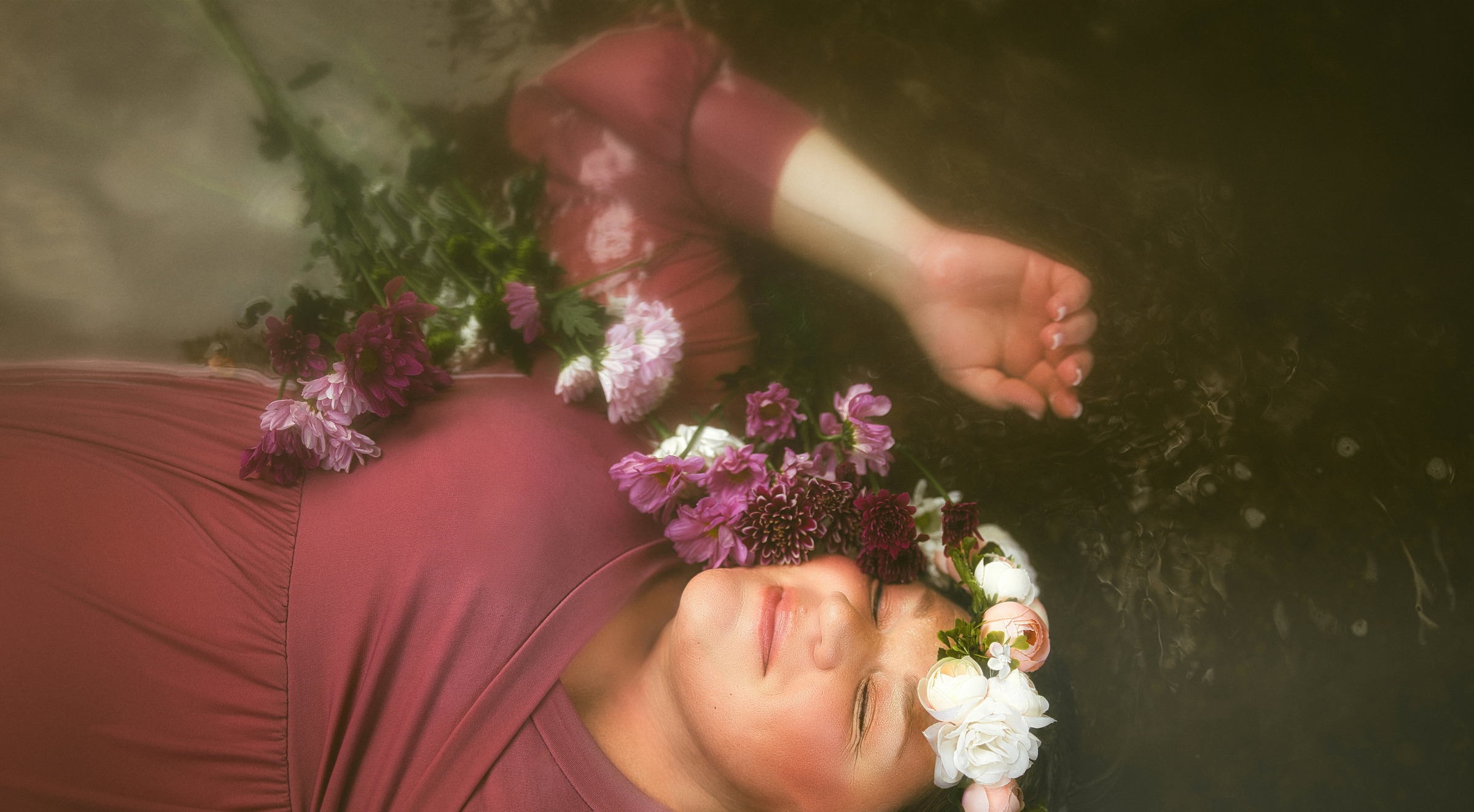 A mother-to-be wearing a flower crown resting in dark water
